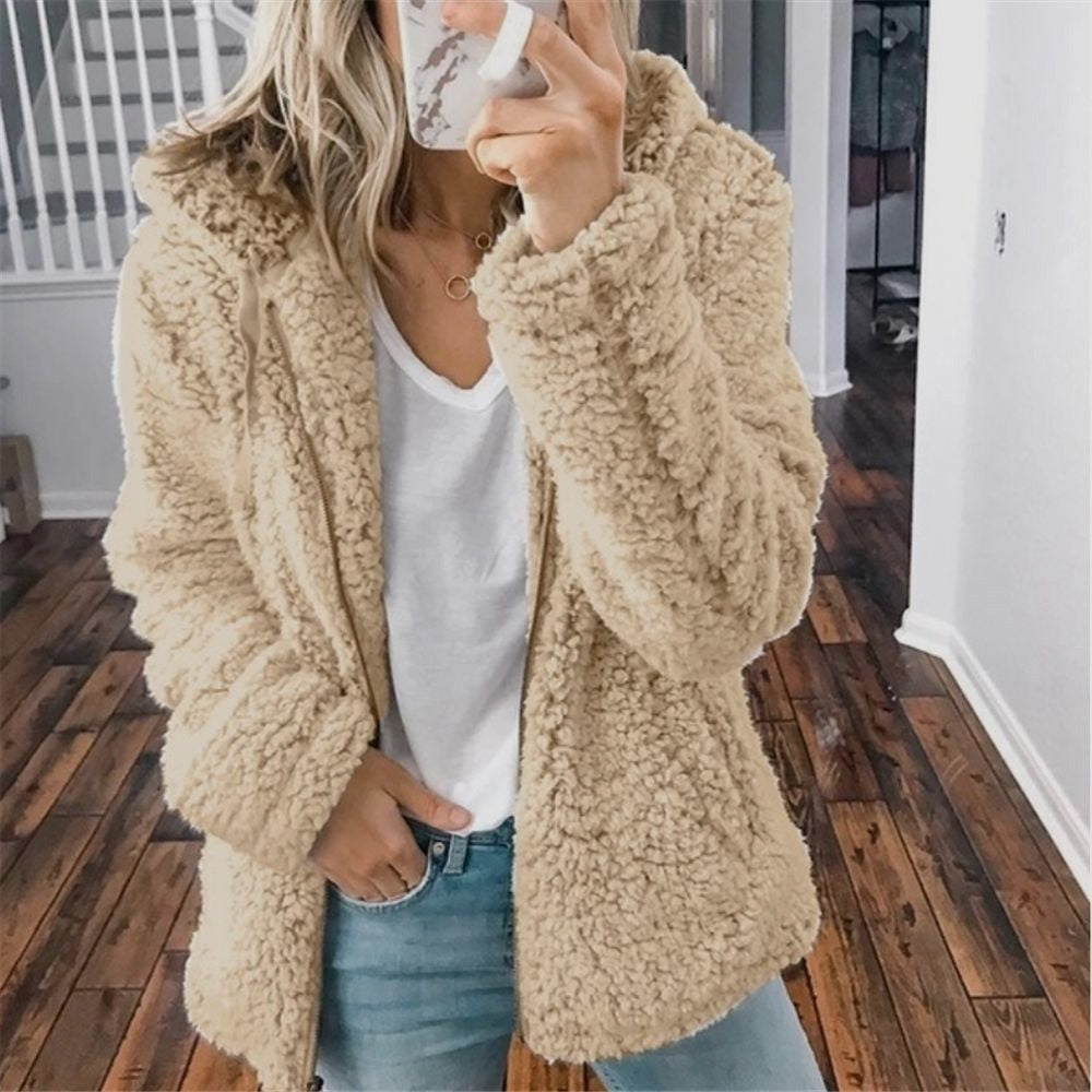 Frau in beigem Teddyfellmantel, weißem T-Shirt und Jeans, Smartphone in der Hand.