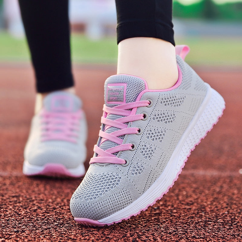 Graue Damen-Laufschuhe mit rosa Schnürsenkeln, atmungsaktiv, auf roter Laufbahn.