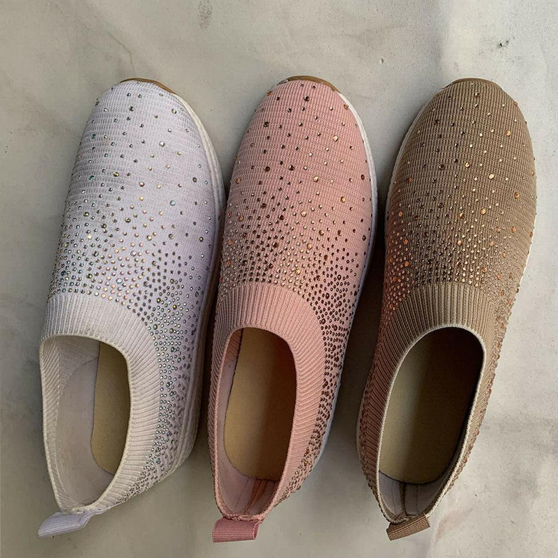 Drei Damen-Sneaker mit Strasssteinen in Weiß, Rosa und Beige auf Marmorhintergrund.