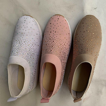 Drei Damen-Sneaker mit Strasssteinen in Weiß, Rosa und Beige auf Marmorhintergrund.