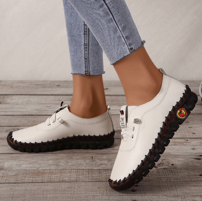 Weiße Damen-Sneaker aus Leder, schwarze Sohle, lässig, bequem, modisch, Jeans-Hintergrund.