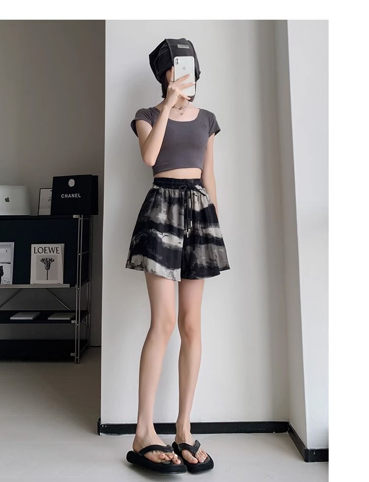 Frau in grauem Crop-Top und schwarz-weißem Rock, trägt schwarze Sandalen, macht Selfie.