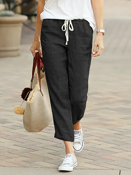 Frau in schwarzer Leinenhose, weiße Sneakers, beige Tasche, lässiger Stil, Straßenmode.