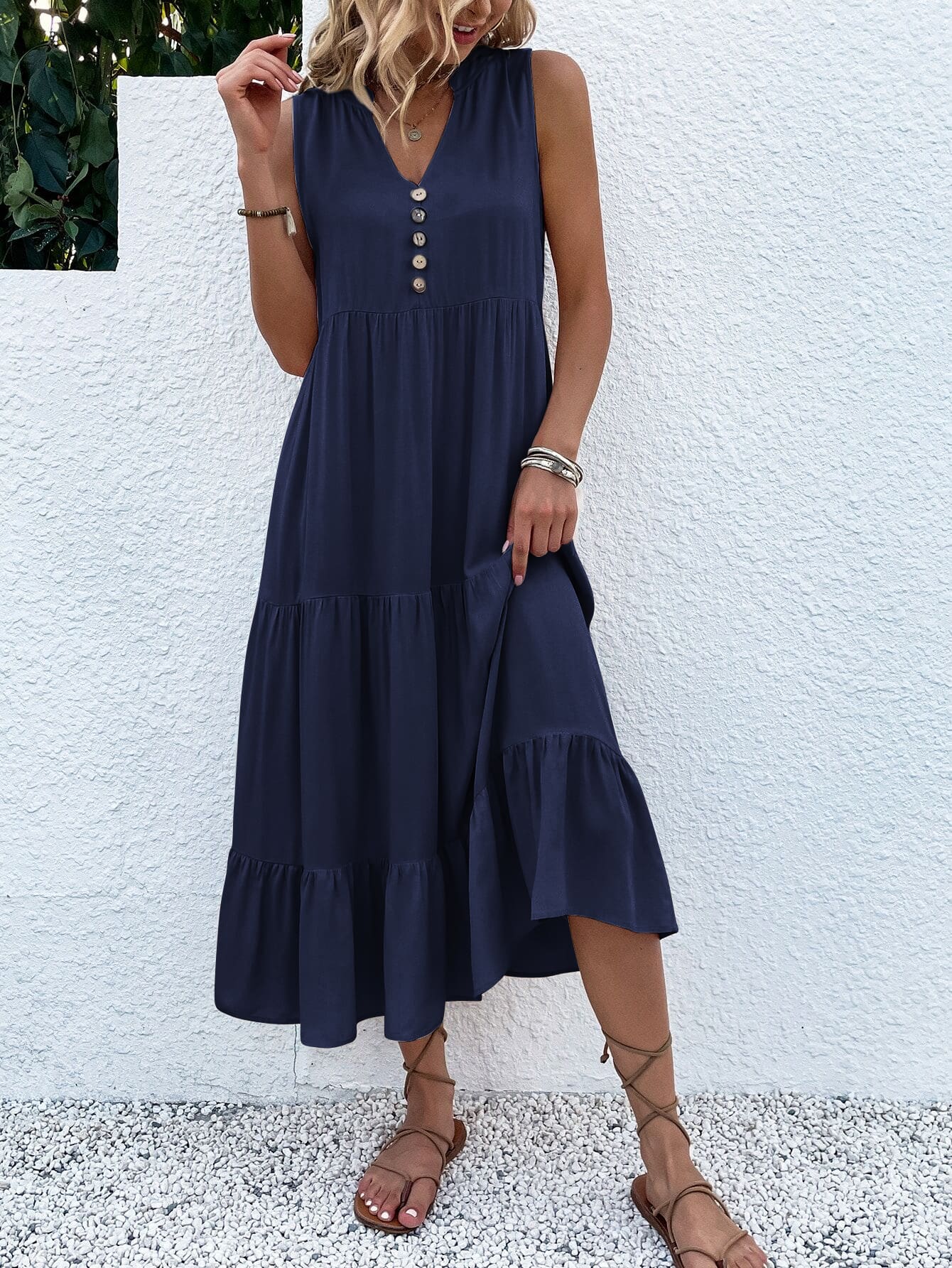 Frau in dunkelblauem Sommerkleid mit Knöpfen, ärmellos, knielang, Sandalen, vor weißer Wand.