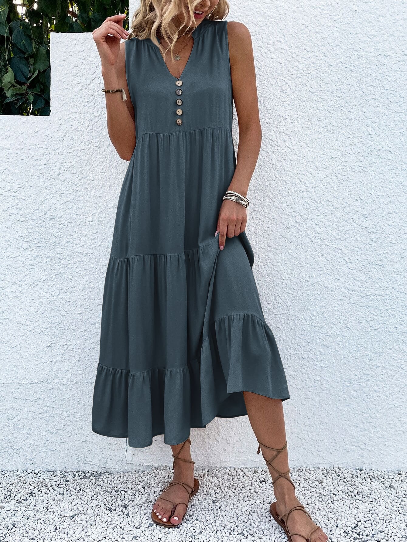 Frau in grauem Sommerkleid mit Knopfleiste, ärmellos, knielang, Sandalen, vor weißer Wand.
