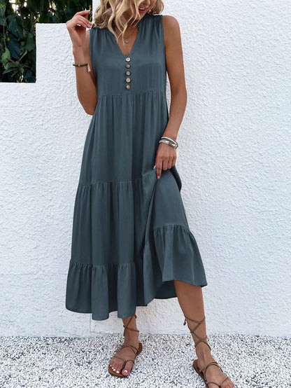 Frau in grauem Sommerkleid mit Knopfleiste, ärmellos, knielang, Sandalen, vor weißer Wand.