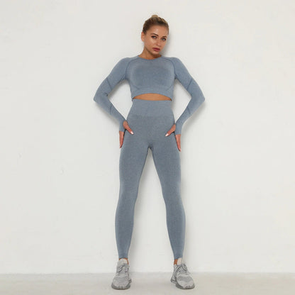 Frau in grauem nahtlosem Sport-Set, Langarm-Top und Leggings, Fitnessmode, vor weißem Hintergrund.