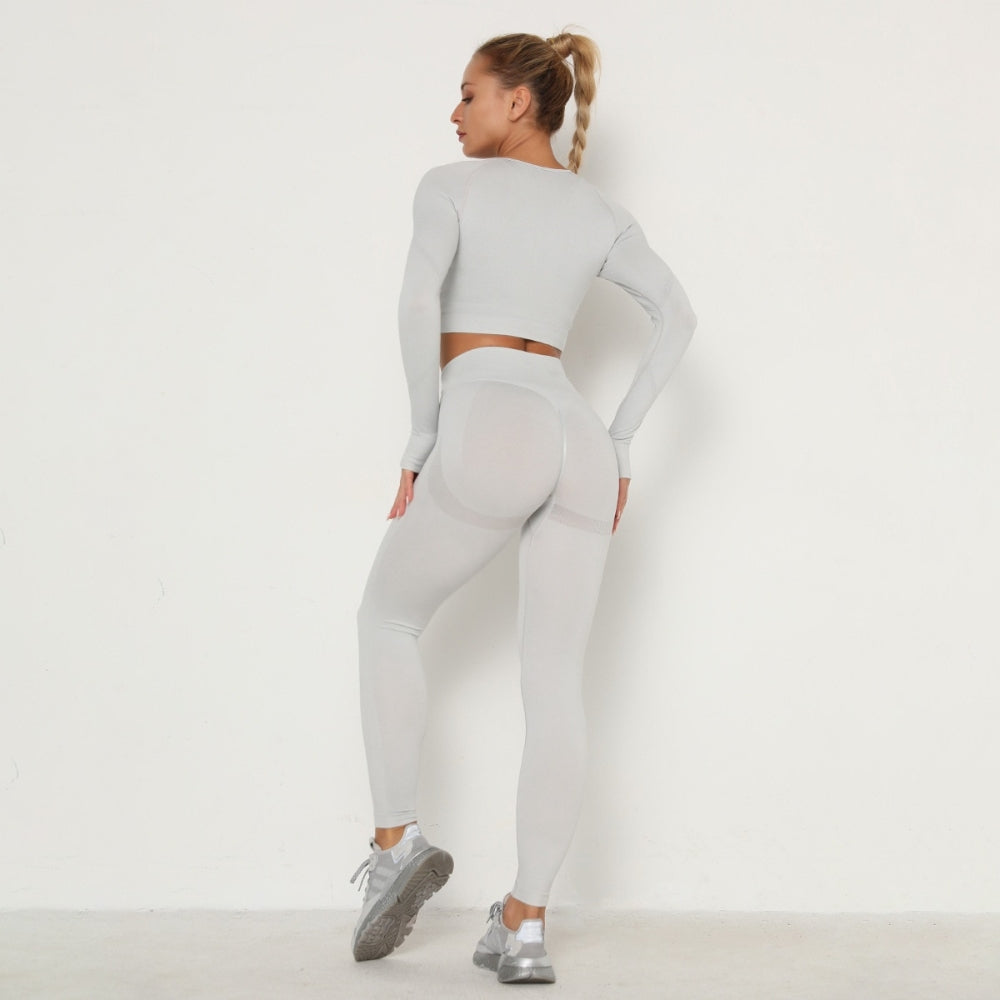 Frau in grauem Sport-Set, langärmeliges Oberteil und Leggings, Fitnessmode, Rückansicht.