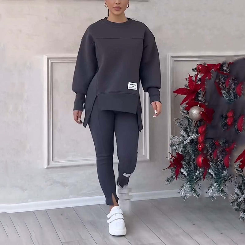Frau in grauem Trainingsanzug, weiße Sneaker, neben weihnachtlich geschmücktem Baum.