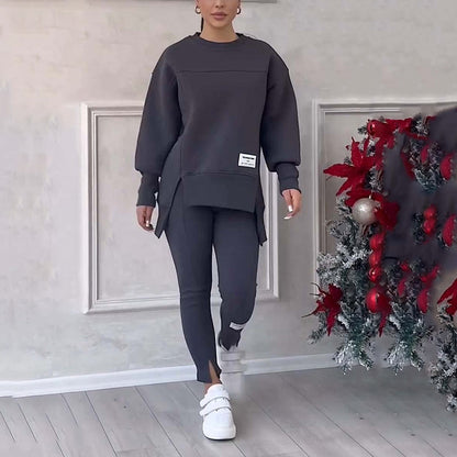 Frau in grauem Trainingsanzug, weiße Sneaker, neben weihnachtlich geschmücktem Baum.