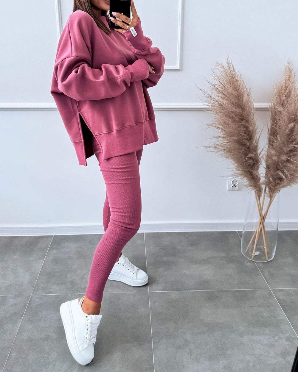 Frau in rosa Oversize-Sweatshirt und Leggings, weiße Sneaker, moderne Freizeitmode.