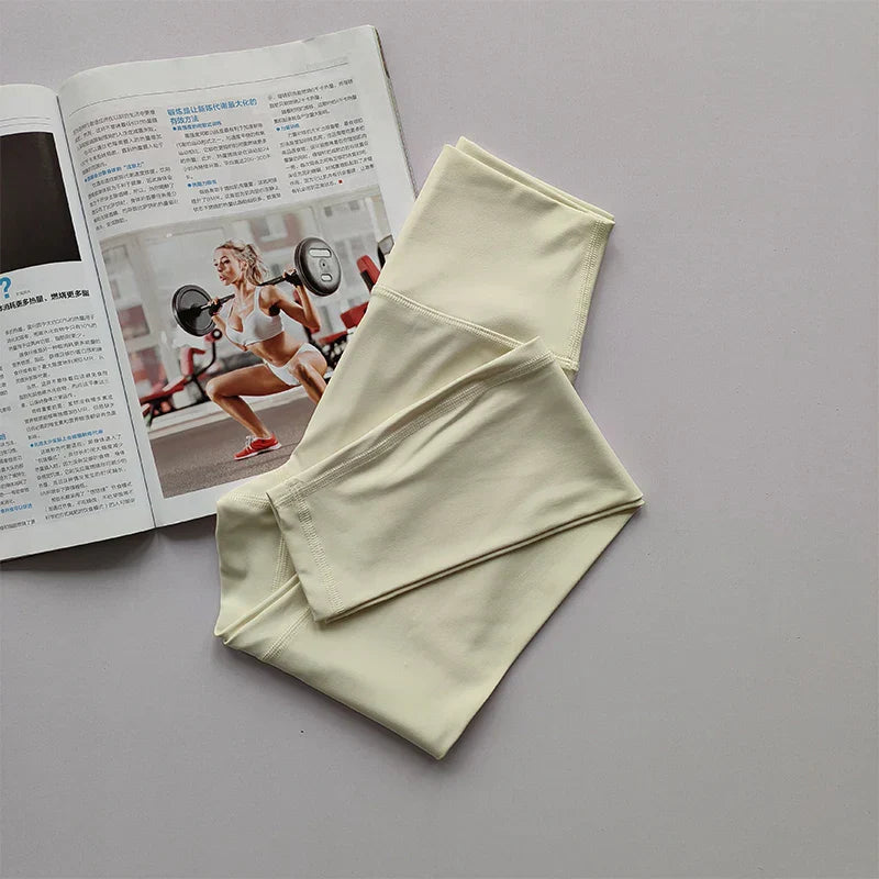 Cremefarbene Leggings aus Baumwolle neben Fitnessmagazin auf grauem Hintergrund.