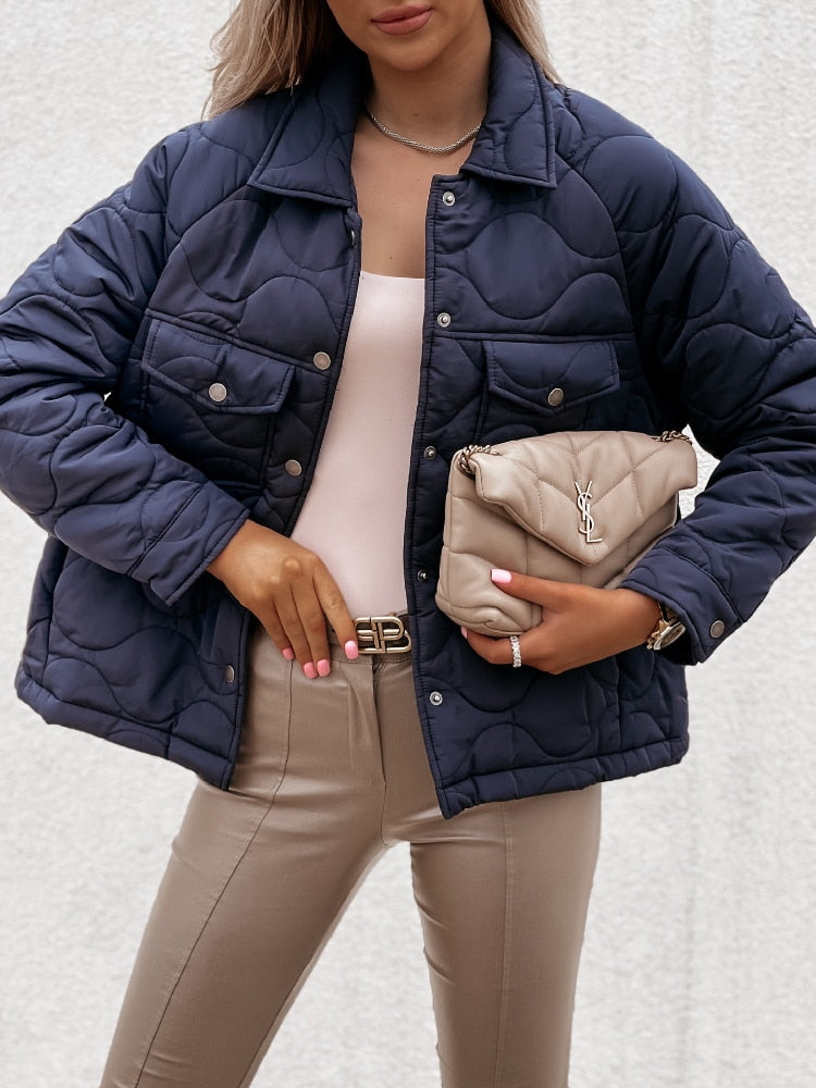 Frau in dunkelblauer Steppjacke, beige Hose, hält Designer-Handtasche, modisch, elegant.