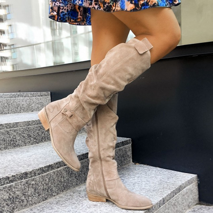 Frau trägt beige Wildleder-Stiefel, kniehoch, modisch, auf Treppe, Stadtumgebung.