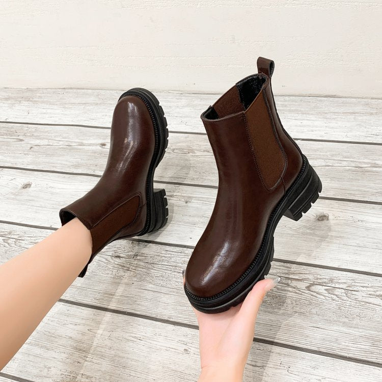 Braune Chelsea-Boots aus Leder mit Profilsohle auf Holzboden.