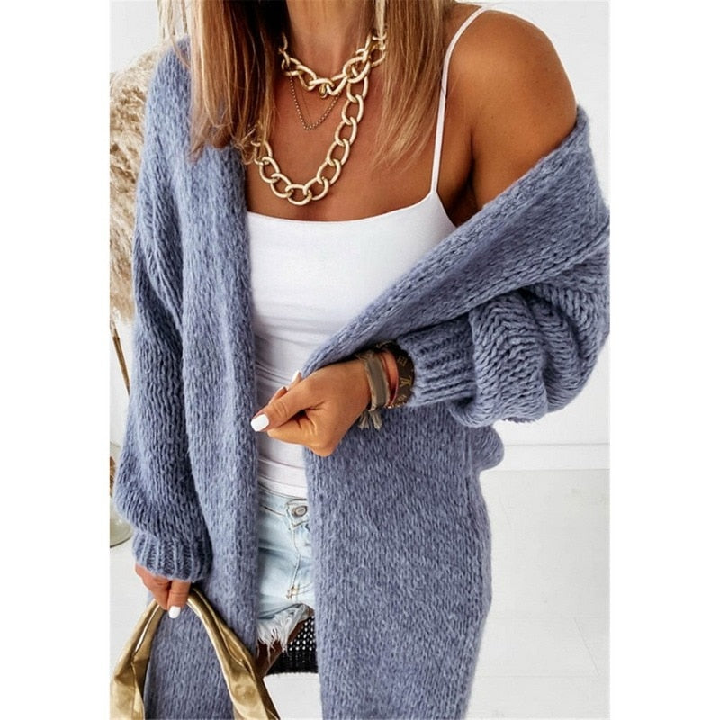Frau in blauem Strickcardigan, weißem Top, Jeansshorts, goldene Kette, modisch, lässig.