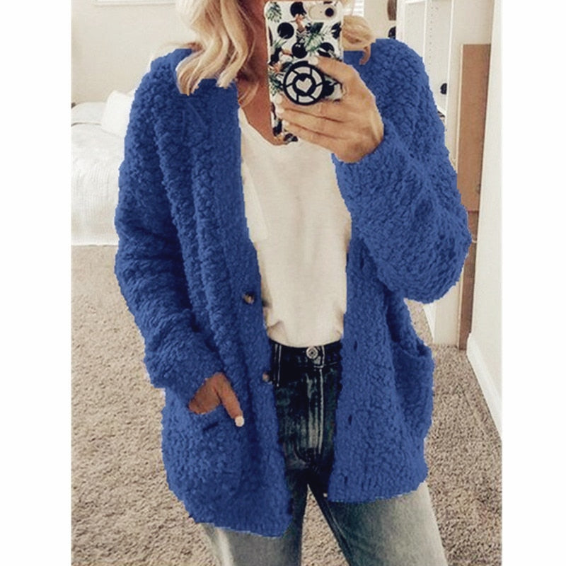 Frau in blauem Strickcardigan, weißem T-Shirt, Jeans, Smartphone, Spiegel-Selfie.