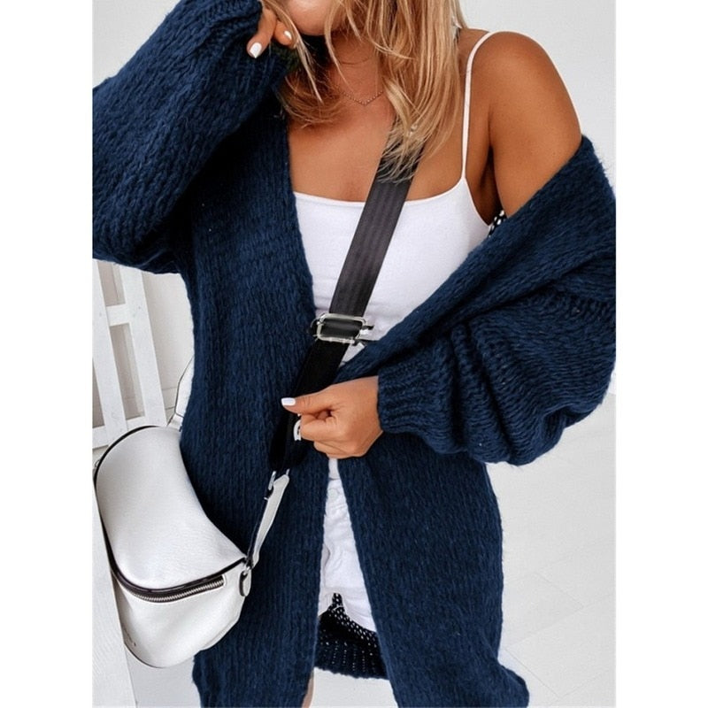 Frau in dunkelblauer Strickjacke, weißem Top, mit weißer Umhängetasche, modisch, lässig.