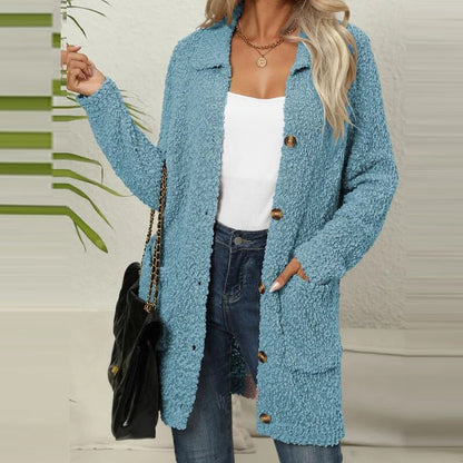 Frau trägt hellblauen Strickmantel, weiße Bluse, Jeans, goldene Kette, schwarze Tasche.