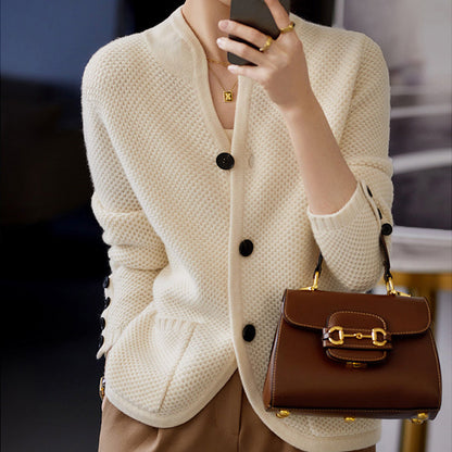 Frau in cremefarbener Strickjacke mit brauner Ledertasche und Smartphone.
