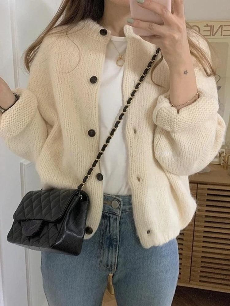 Frau in cremefarbenem Strick-Cardigan, weiße Bluse, Jeans, schwarze Umhängetasche.