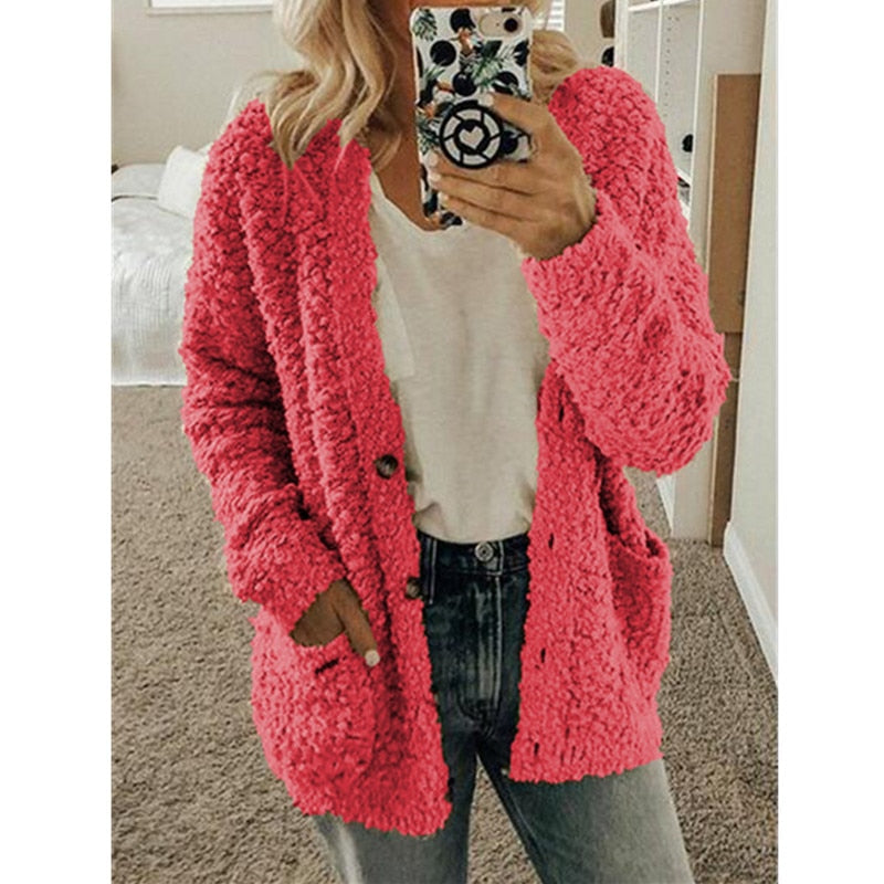 Frau in rosa Strickjacke, Handyhülle mit Muster, lässiger Look, gemütliches Wohnzimmer.