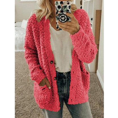Frau in rosa Strickjacke, Handyhülle mit Muster, lässiger Look, gemütliches Wohnzimmer.