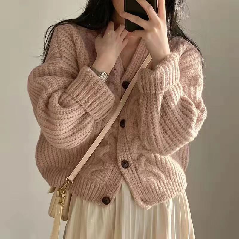 Frau in rosa Strickjacke mit Knöpfen, cremefarbenem Rock und beiger Umhängetasche.