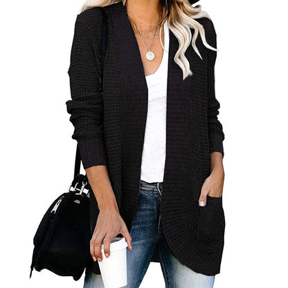 Frau in schwarzer Strickjacke, weißem T-Shirt, Jeans, mit Kaffeebecher und schwarzer Tasche.