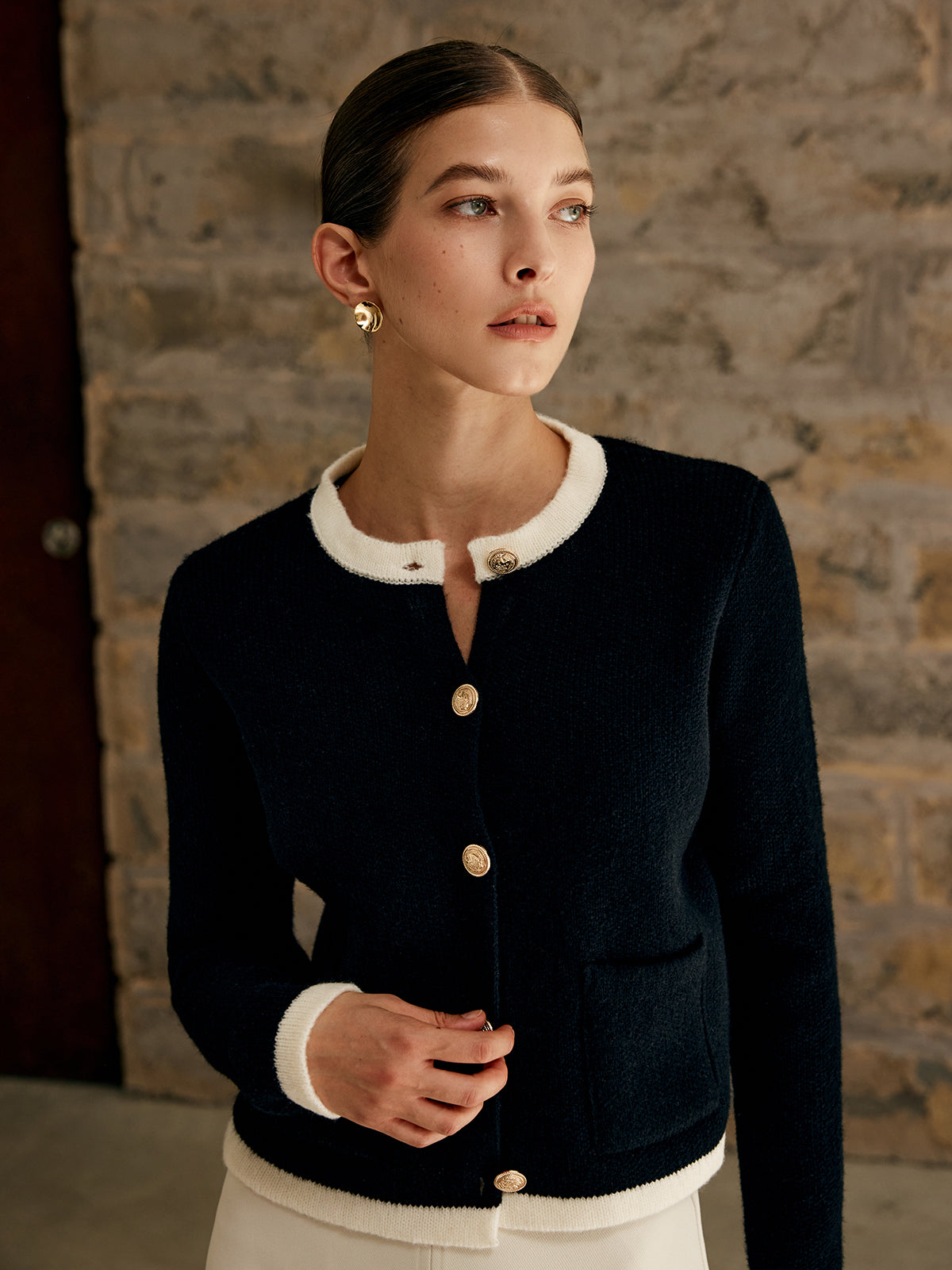 Frau in schwarzer Strickjacke mit weißen Details vor Steinwand, elegante Mode, Herbstkollektion.