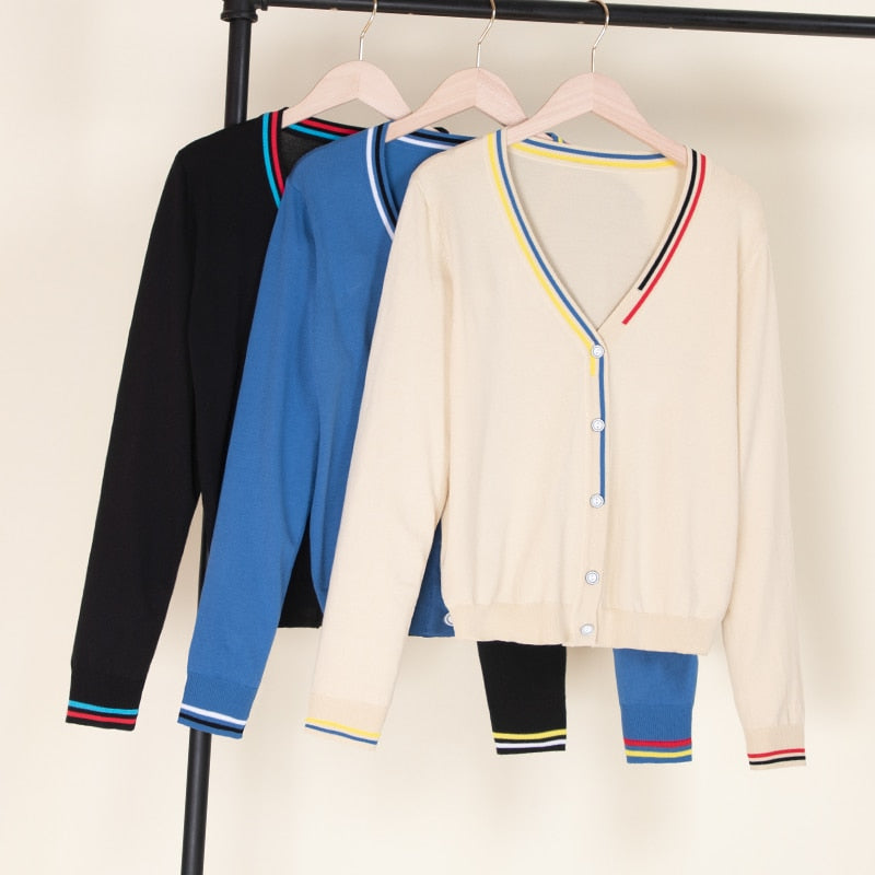 Drei Damen-Cardigans, V-Ausschnitt, schwarz, blau, creme, gestreifte Details, auf Kleiderbügeln.