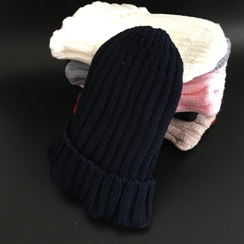 Schwarze Strickmütze aus Wolle, gestapelt mit bunten Mützen, Wintermode Accessoire.