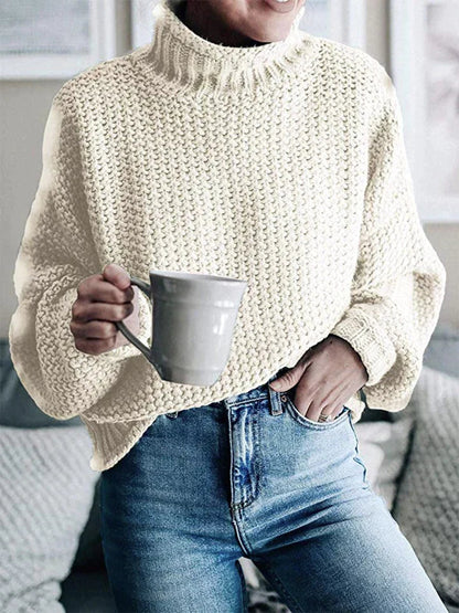 Frau in cremefarbenem Strickpullover hält graue Tasse, trägt blaue Jeans.
