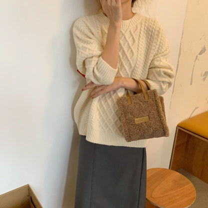 Frau in cremefarbenem Strickpullover mit brauner Plüschhandtasche, modisch, elegant.