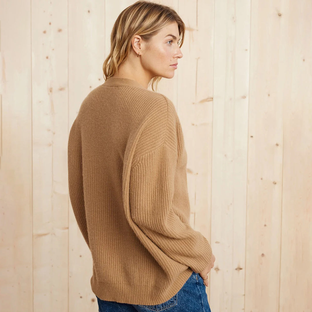 Frau in beigem Strickpullover aus Wolle, seitlich, vor Holzwand, lässige Mode, Herbstlook.