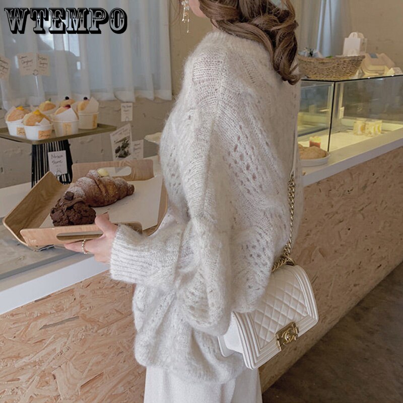 Frau in weißem Strickpullover mit weißer Umhängetasche in einem Café.