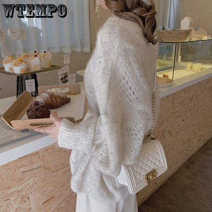 Frau in weißem Strickpullover mit weißer Umhängetasche in einem Café.
