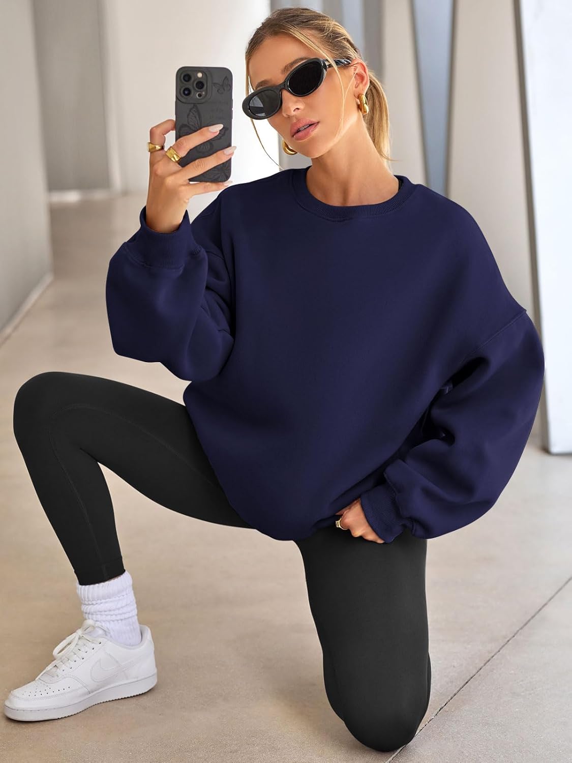 Frau in dunkelblauem Oversize-Pullover, schwarze Leggings, weiße Sneaker, Sonnenbrille, Selfie.