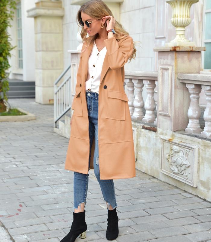 Frau in beigem Trenchcoat, weiße Bluse, zerrissene Jeans, schwarze Stiefeletten, Sonnenbrille.