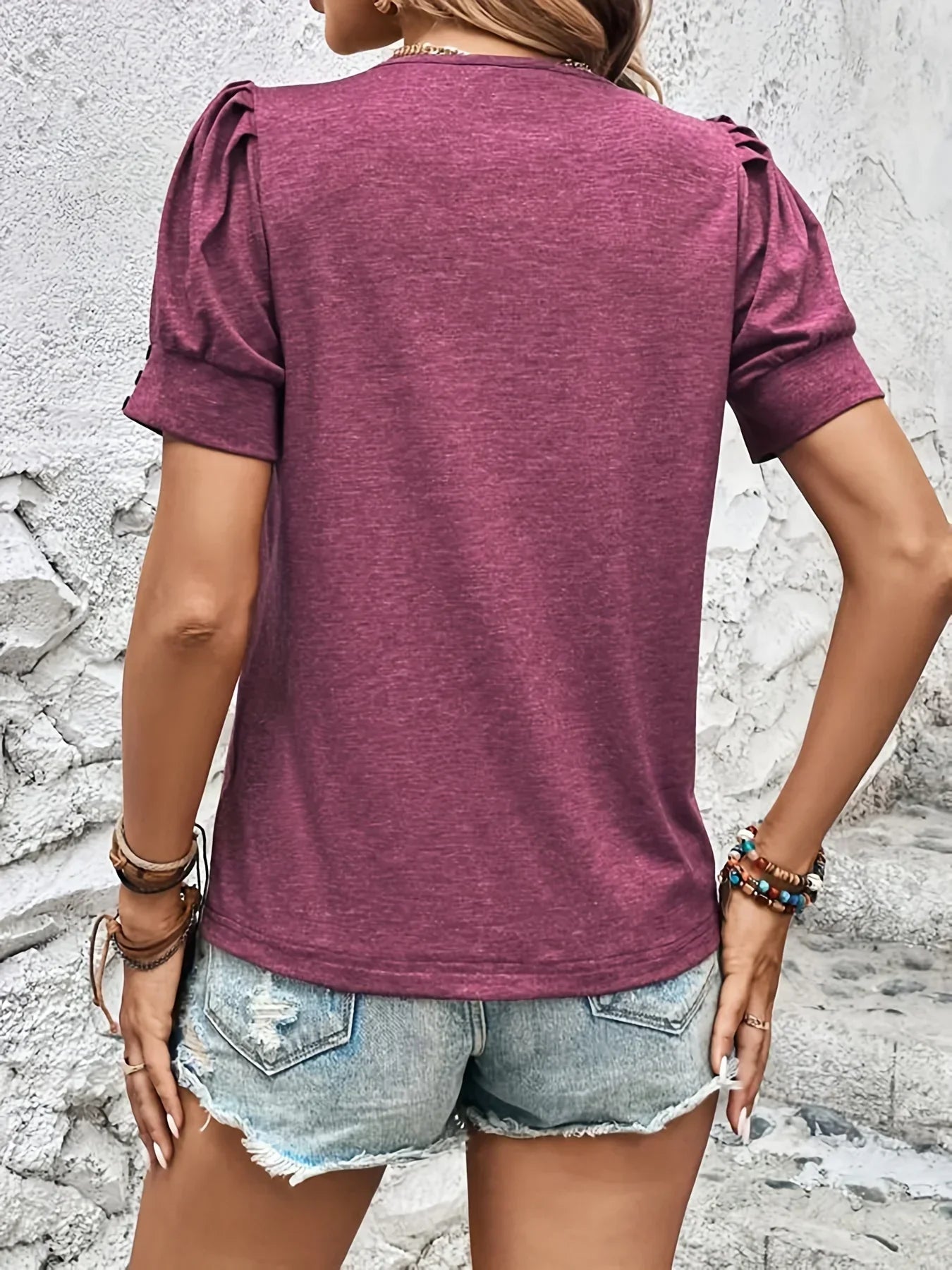 Frau in lila T-Shirt und Jeansshorts vor weißer Wand, Sommermode, Freizeitkleidung.
