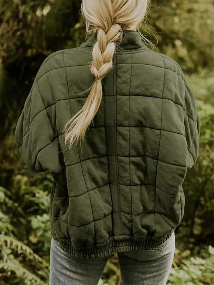 Frau in olivgrüner, gesteppter Übergangsjacke mit Zopf im Wald.