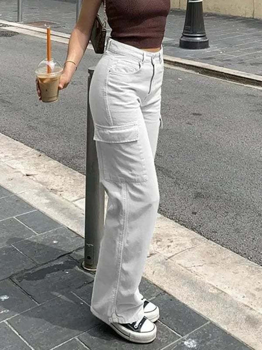 Frau in weißen Cargo-Hosen und braunem Top mit Eiskaffee auf Gehweg.