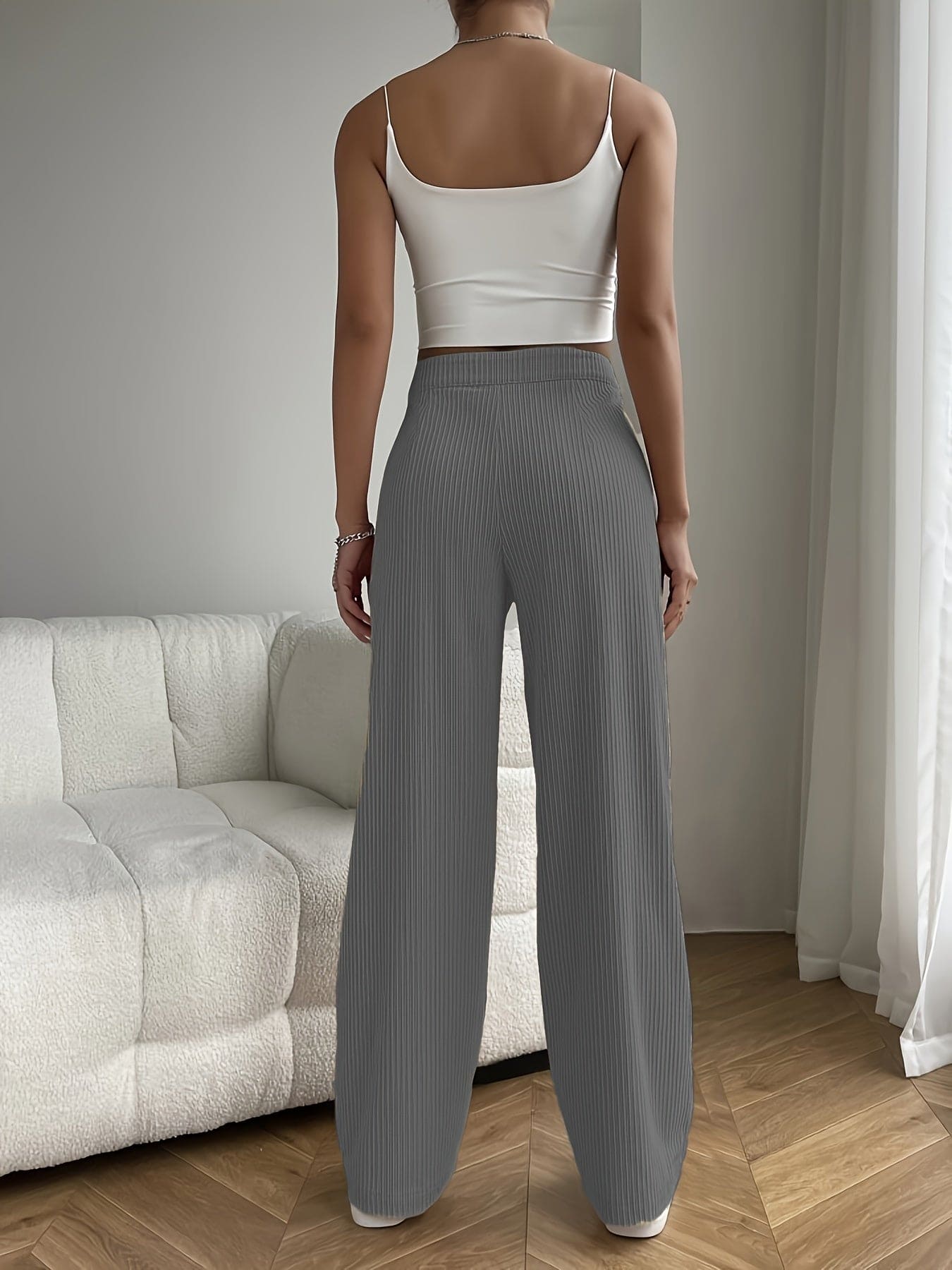 Frau in weißem Top und grauer Hose, steht vor einem weißen Sofa in modernem Wohnzimmer.