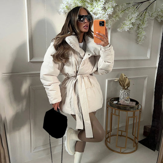 Frau in weißem Daunenmantel mit Gürtel, Sonnenbrille, Handy, modisch, Wintermode, Innenraum.