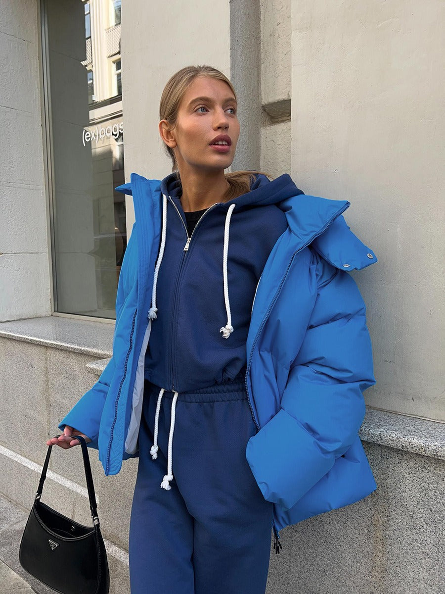 Frau in blauer Daunenjacke und Jogginganzug, hält schwarze Handtasche, Stadtumgebung.
