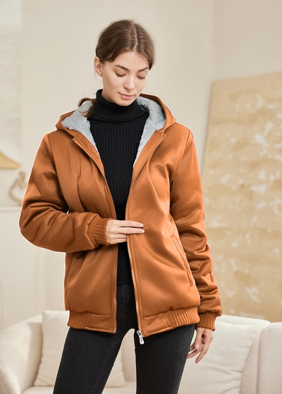 Frau in brauner Kapuzenjacke, schwarzem Rollkragenpullover, gemütliche Wintermode, Innenraum.