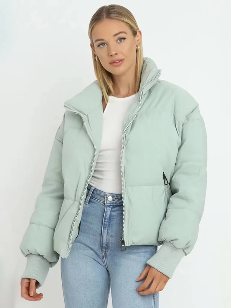 Frau in mintgrüner Daunenjacke, weiße Bluse, blaue Jeans, modisch, Winterkleidung.