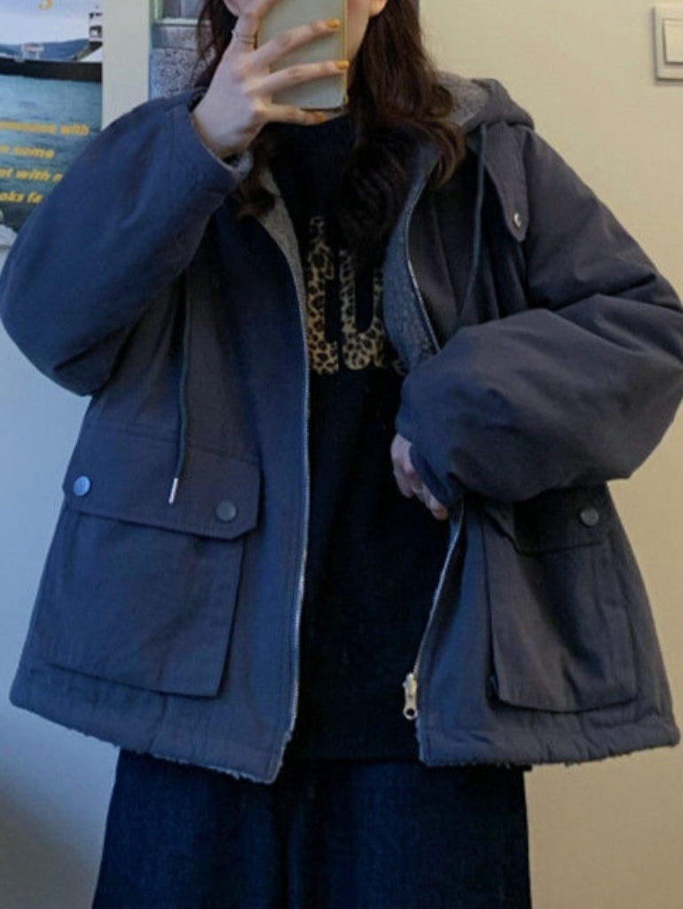 Frau in dunkelblauer Winterjacke mit Kapuze, hält Smartphone, modisch, warm, Outdoor-Bekleidung.