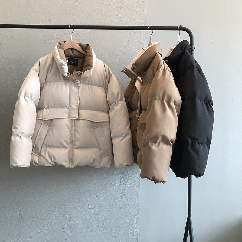 Drei Daunenjacken in Weiß, Beige und Schwarz auf Kleiderstange, Wintermode, warm, stilvoll.