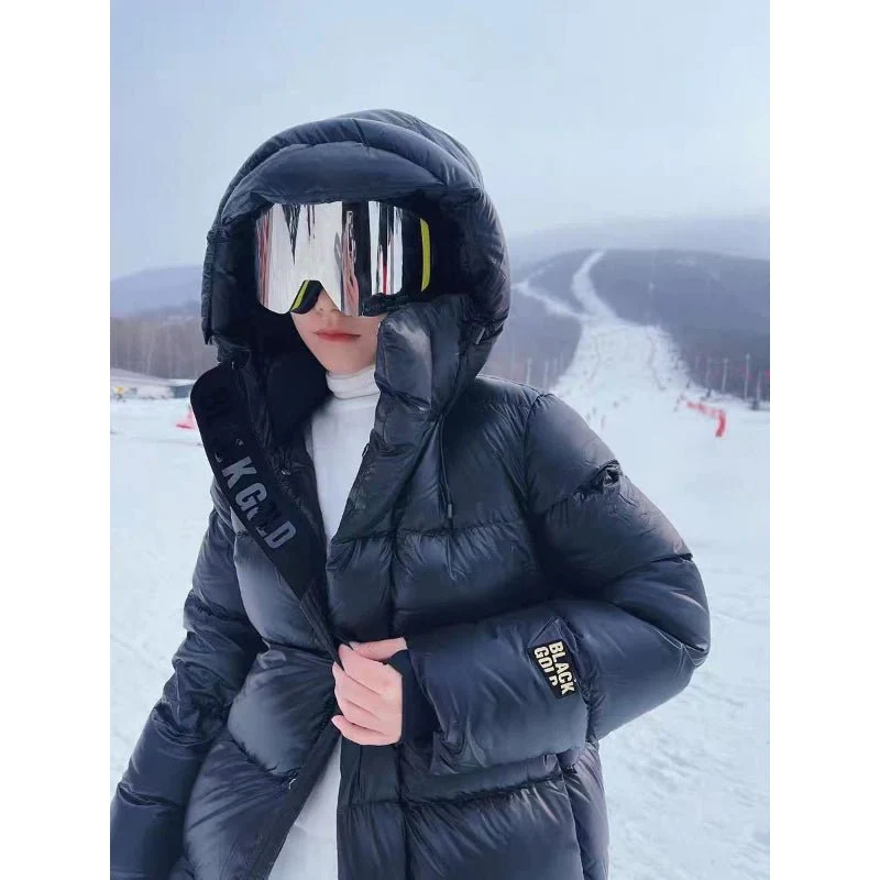 Frau in schwarzer Daunenjacke mit Kapuze und Skibrille auf verschneiter Skipiste.